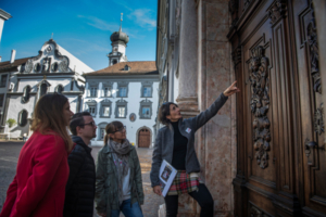 Stadtführerin zeigt 3 Personen das Kirchenportal